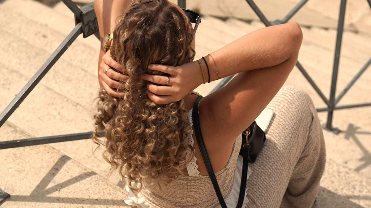 Femme aux longues boucles blondes, de dos, les mains dans les cheveux